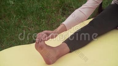 孕妇在公园里的地毯上做瑜伽，一条腿伸着坐着，做一个手对脚的倾斜。